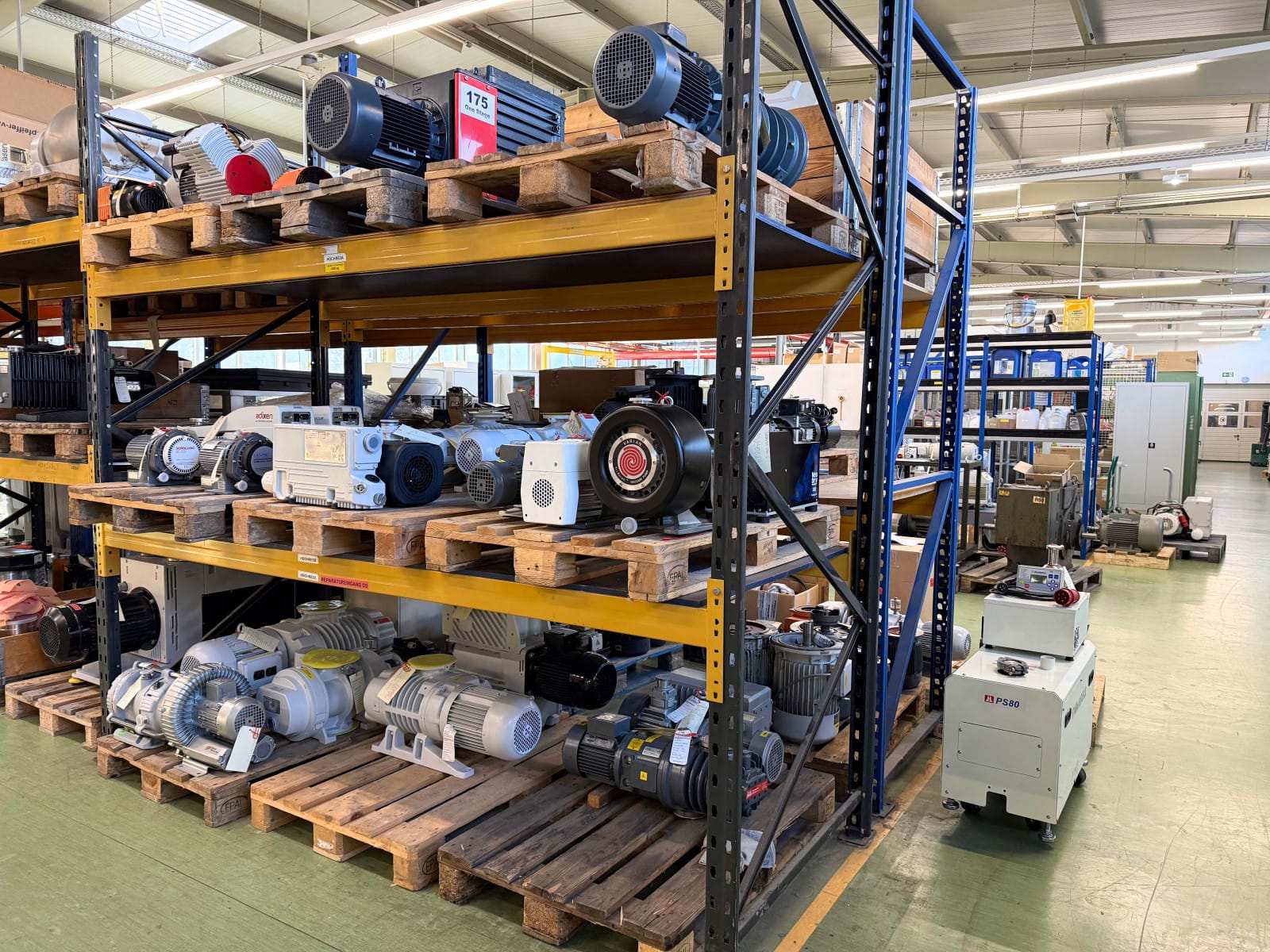 Mehrstöckiges Schwerlastregal in einer Industriehalle, gefüllt mit verschiedenen gebrauchten Vakuumpumpen und Leihgeräten auf Europaletten.